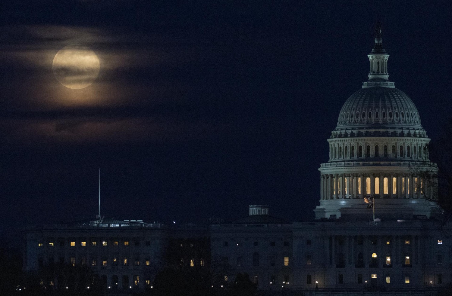 A large orange full Moon rising behind the dome of the U.S. Capitol at dusk